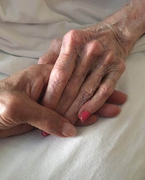 Hand holding a frail, elderly hand.