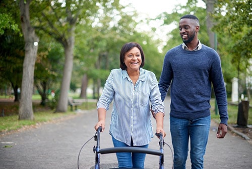 A happy mature woman using a walker while a handsome young man assists her in the park.